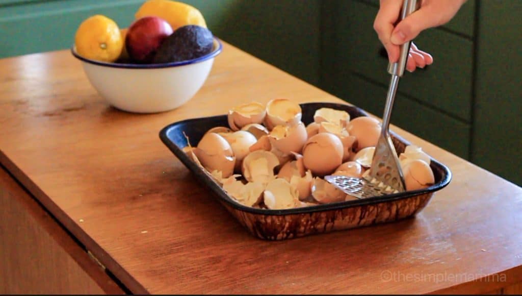 baked egg shells in a baking dish being mashed with a potato masher